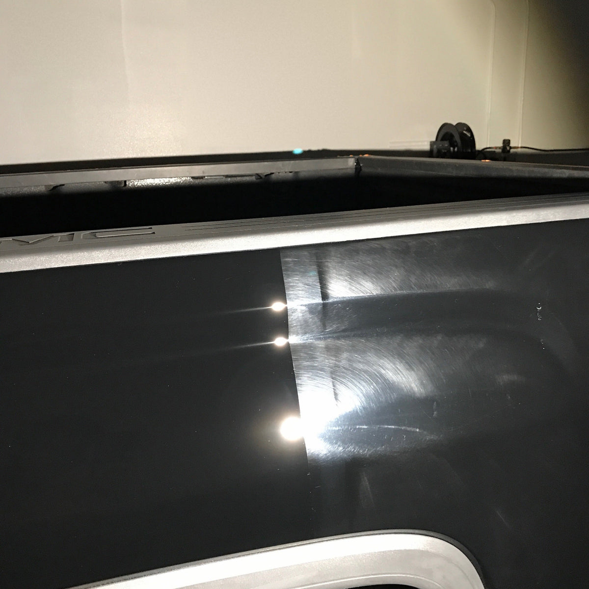 Before and after paint correction on a black truck bed showing swirl removal